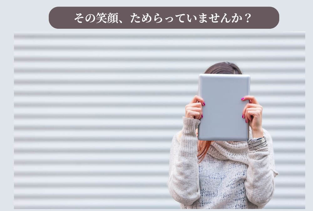 恥ずかしそうにタブレットで顔を隠している女性。